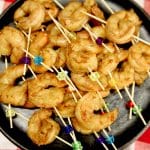 Shrimp on appetizer picks on a black plate.