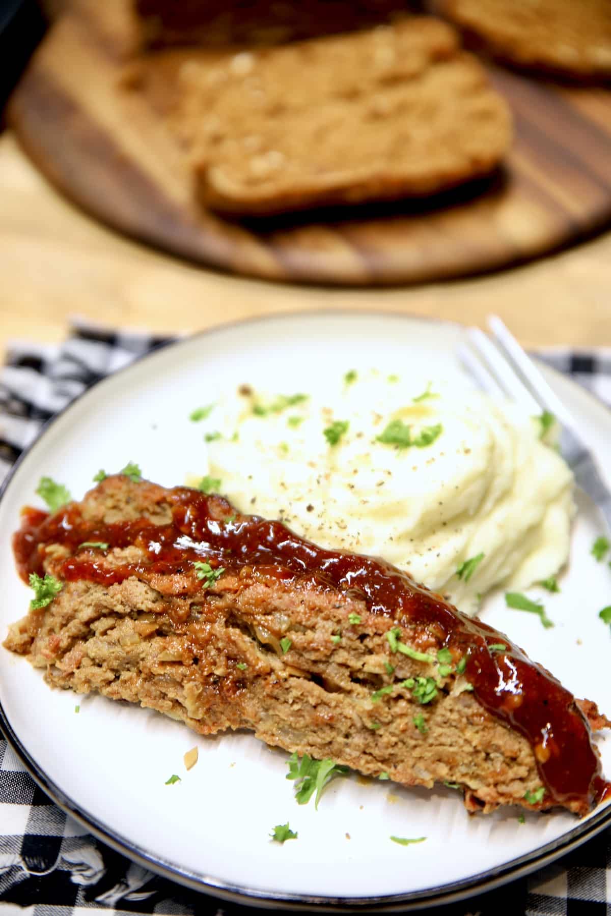 Sliced meatloaf with bbq sauce on a plate with mashed potatoes.