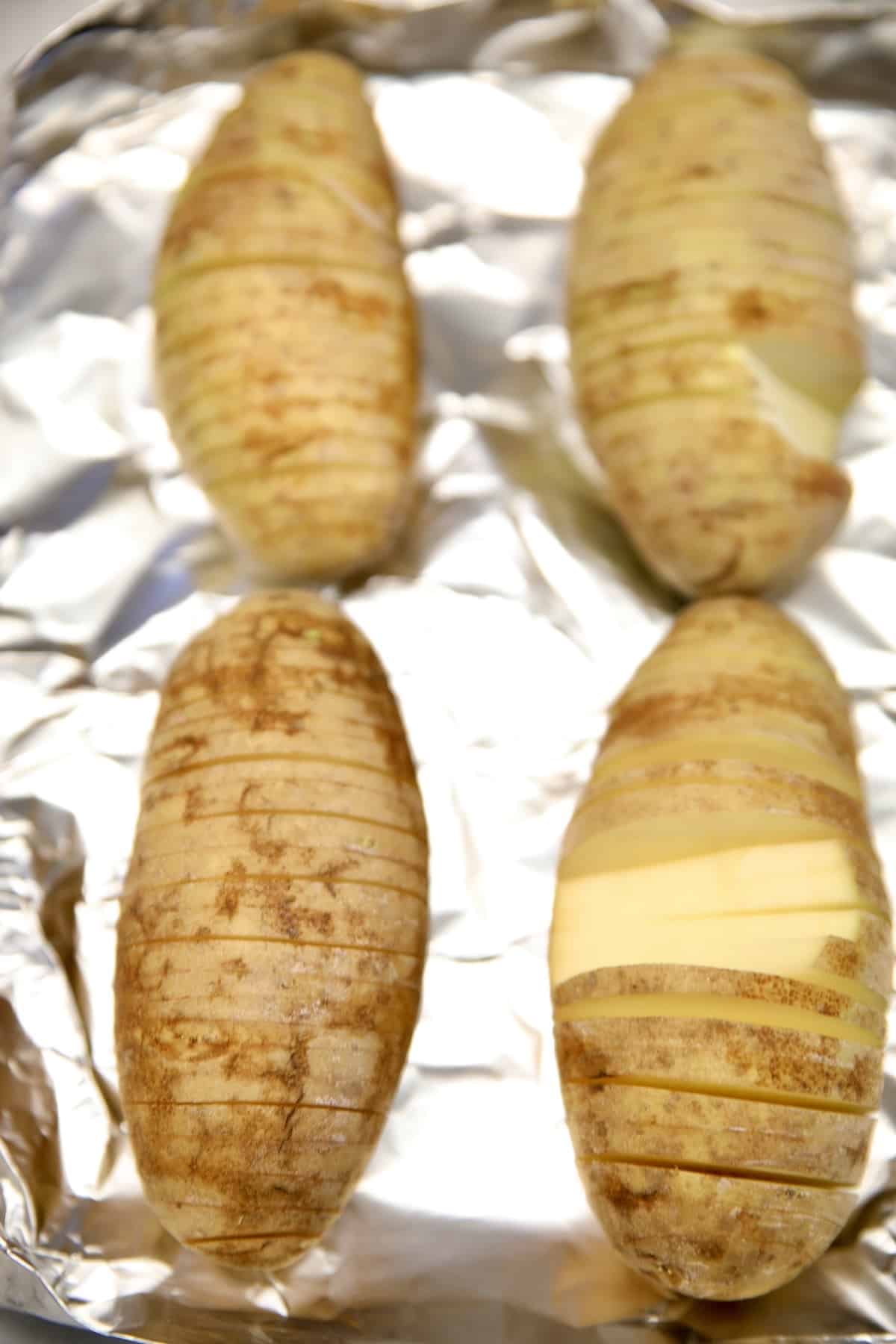 Hasselback russet potatoes on a foil lined baking sheet.