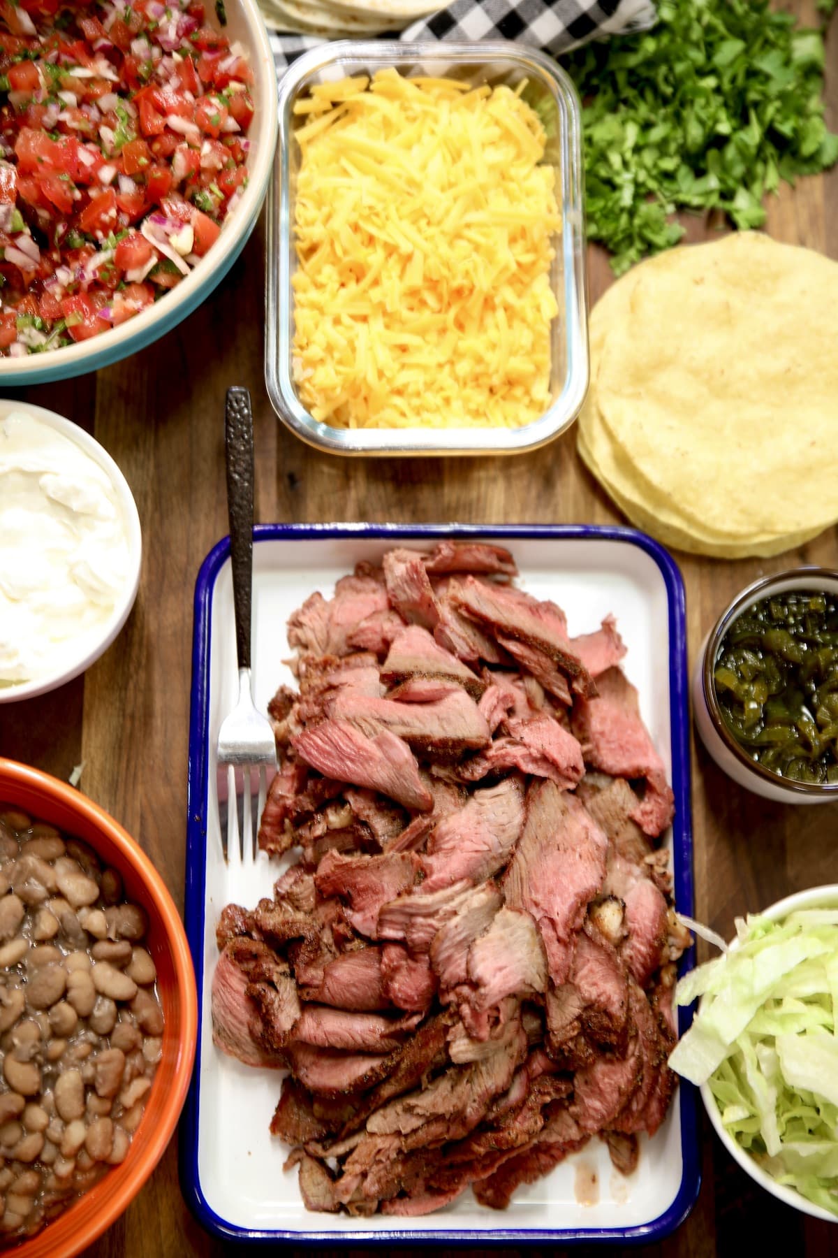 Platter of sliced chuck roast, bowls of taco toppings, taco shells.