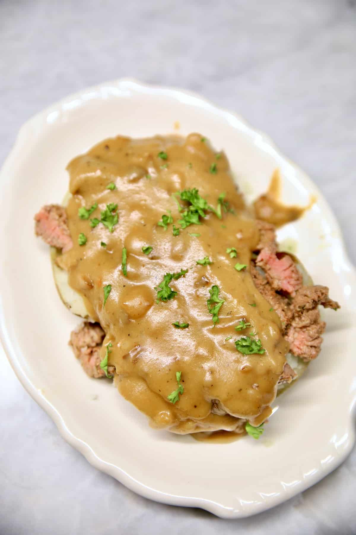 Grilled cube steak and gravy over baked potato on a plate.