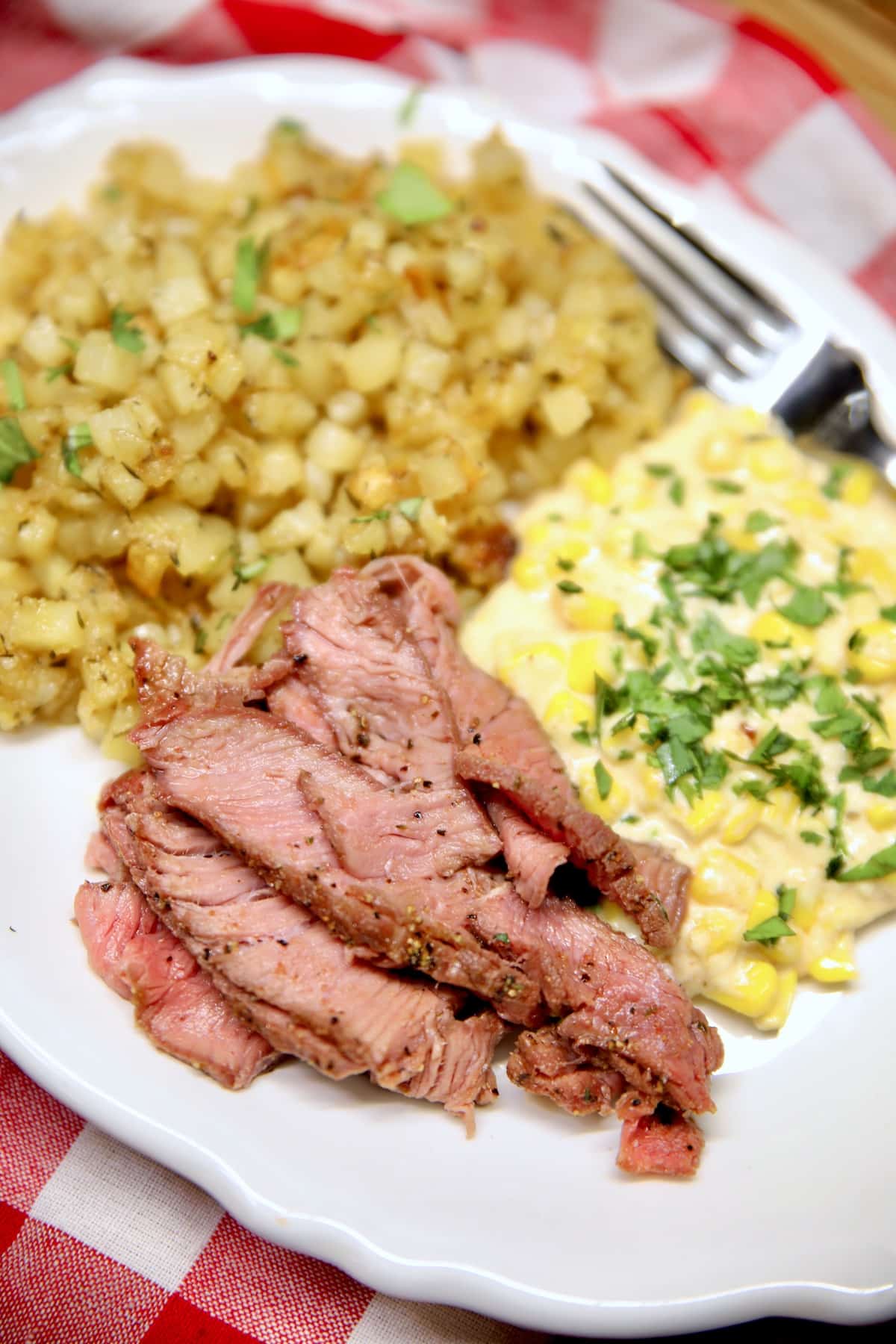 Sirloin Steak sliced on a plate with potatoes and corn.