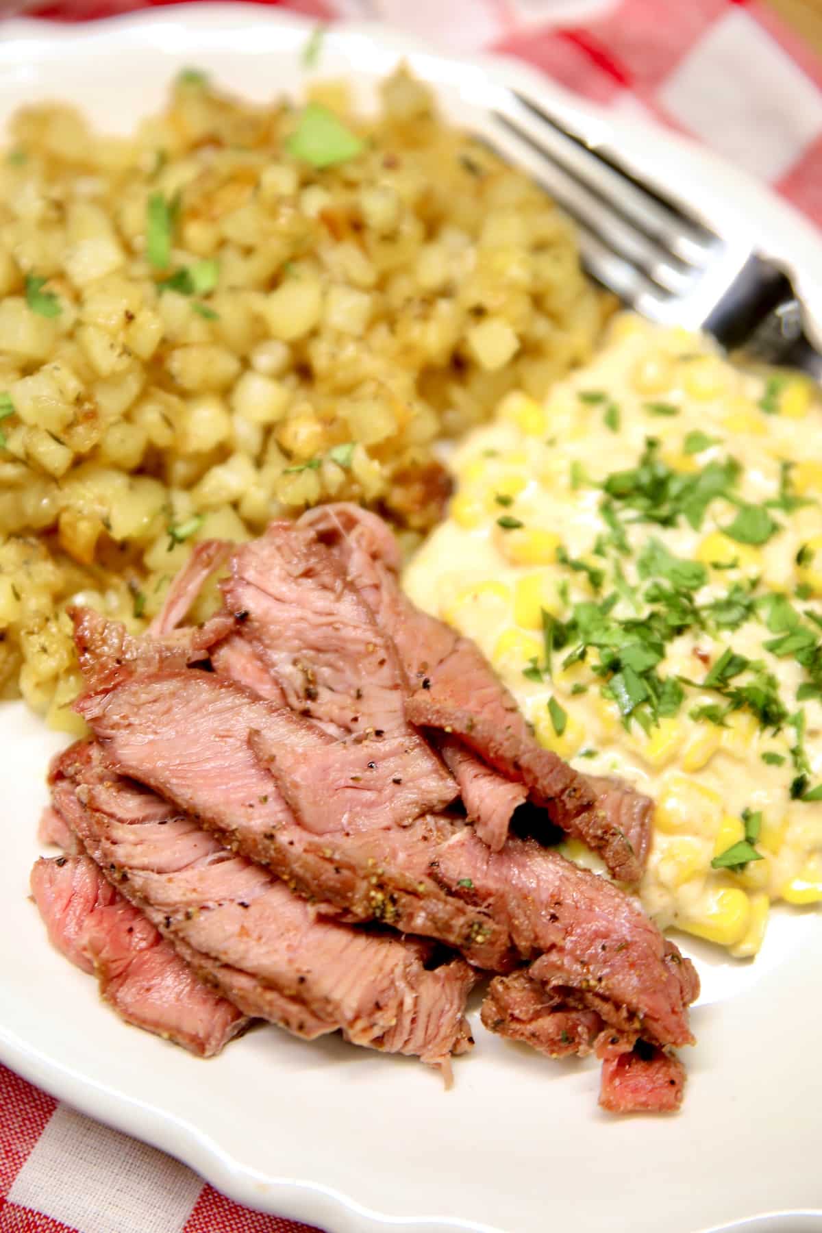 Sirloin steak sliced on a plate with potatoes and corn.