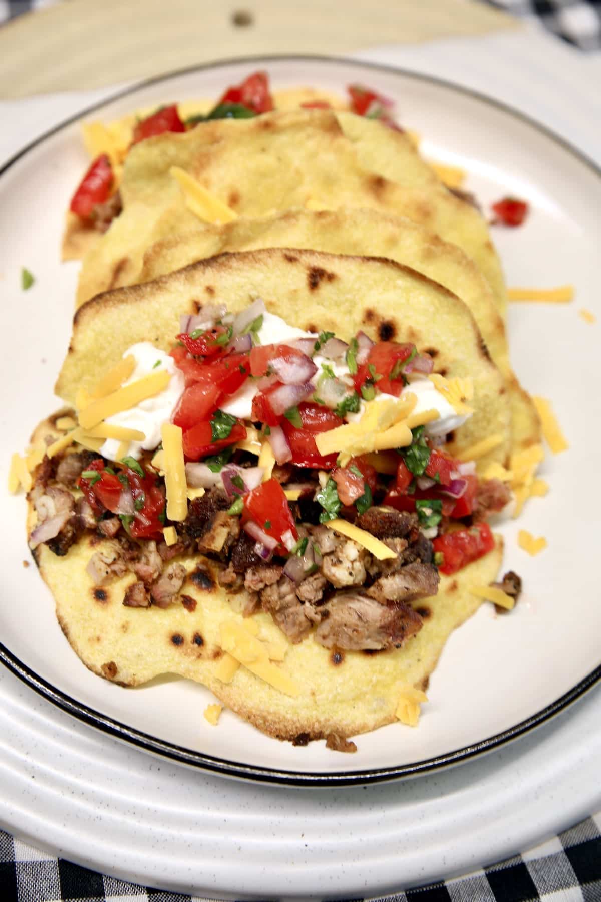 Beef tacos on a plate with salsa, cheese and sour cream.