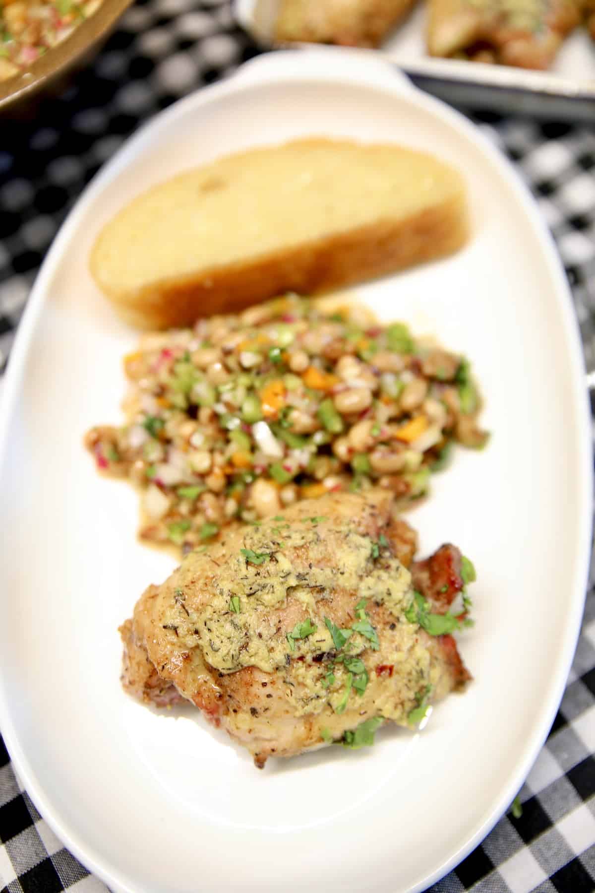 Garlic butter chicken thigh, black eyed pea salad and bread on a platter.