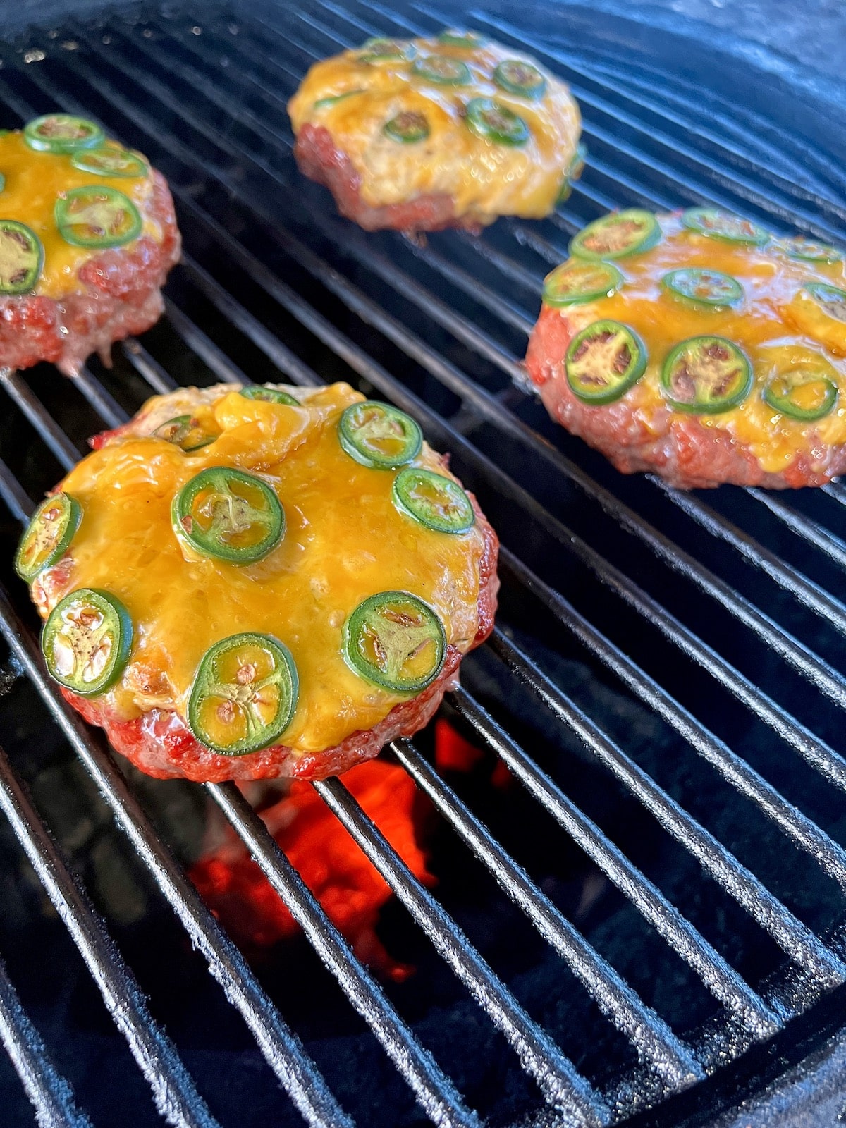 4 burger patties with cheese and jalapenos on a grill.