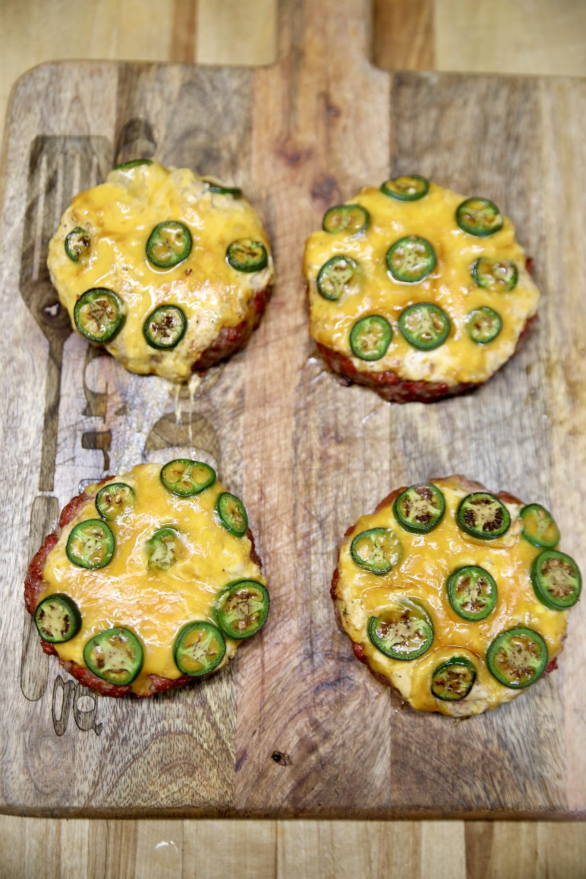 4 grilled jalapeno popper burger patties on a cutting board.