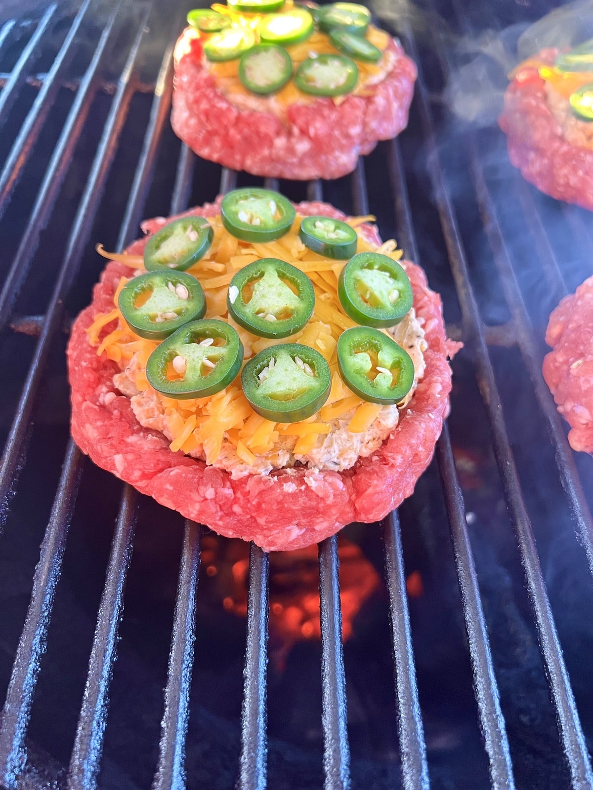 Stuffed burgers on a grill with jalapenos and cheese.