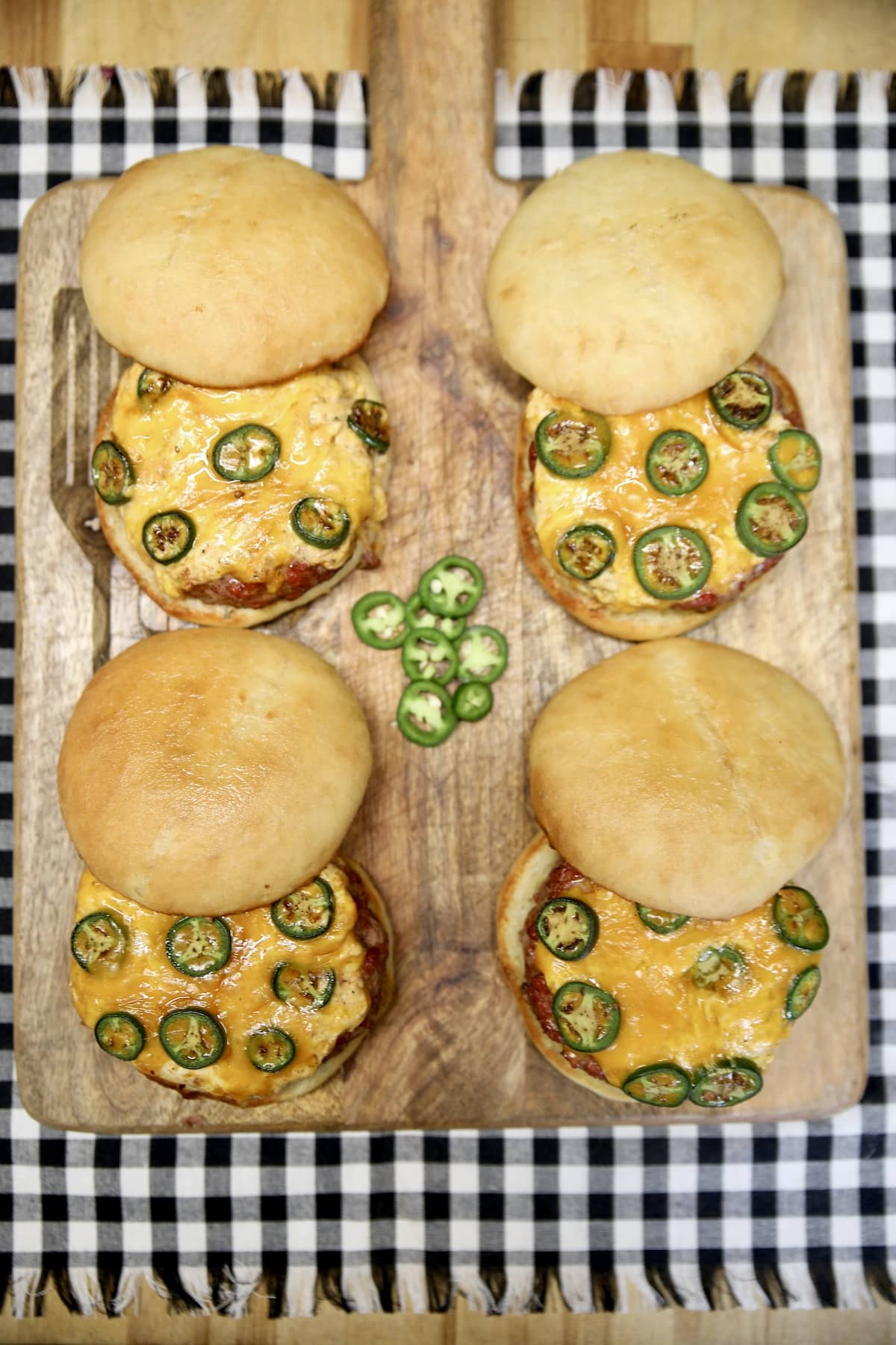 4 burgers with cheese and jalapenos on a board and napkin.