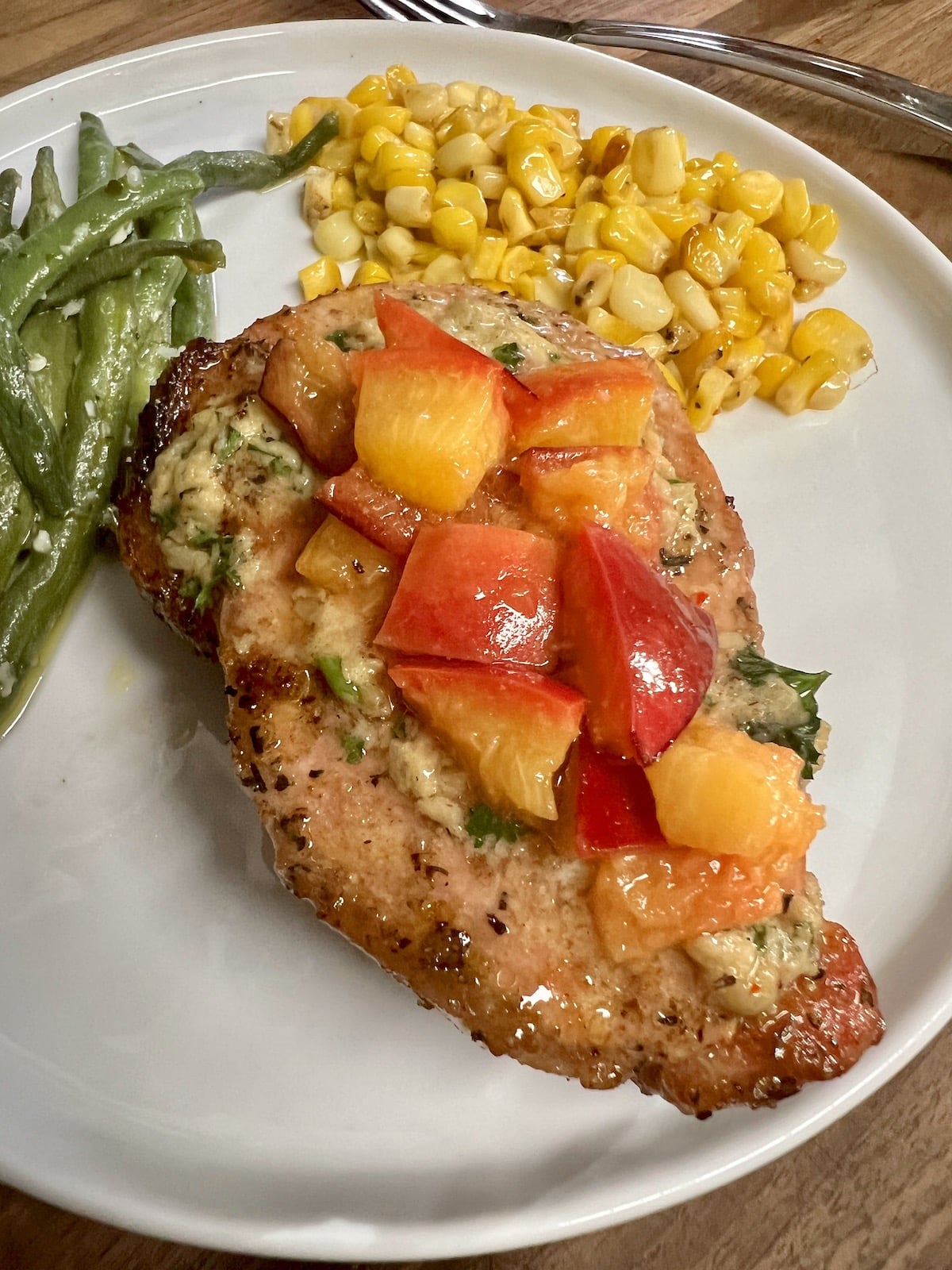 Pork chop on a plate with grilled peaches, corn and green beans.