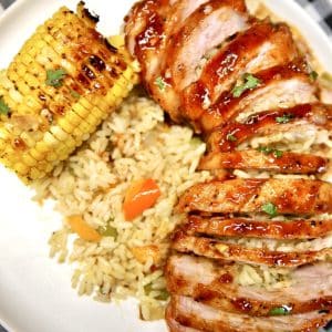 Sliced pork chops stuffed with rice with corn on a plate.