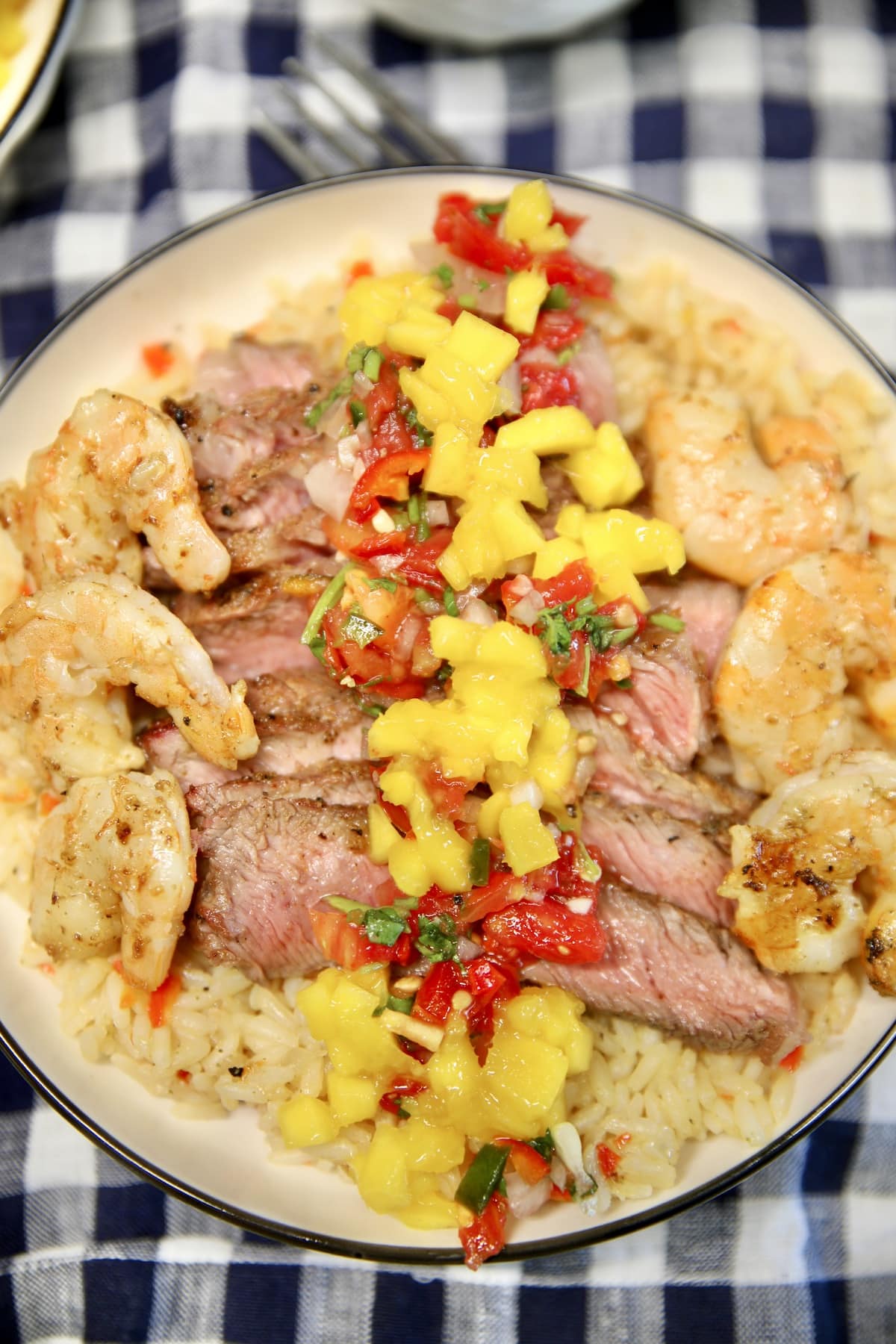 Rice bowl with sliced steak, shrimp, mango and salsa.