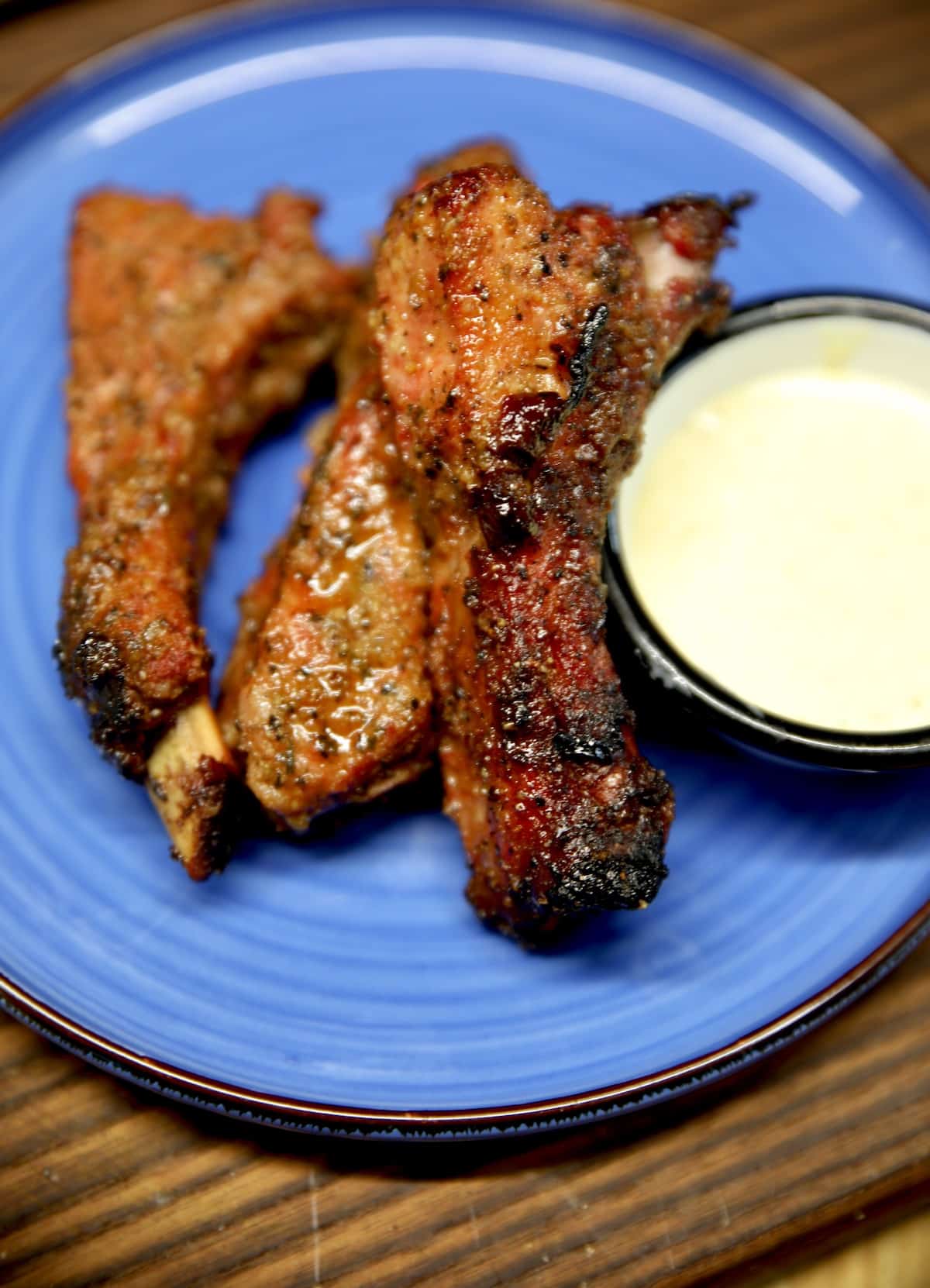 3 baby back ribs on a plate with white bbq sauce.