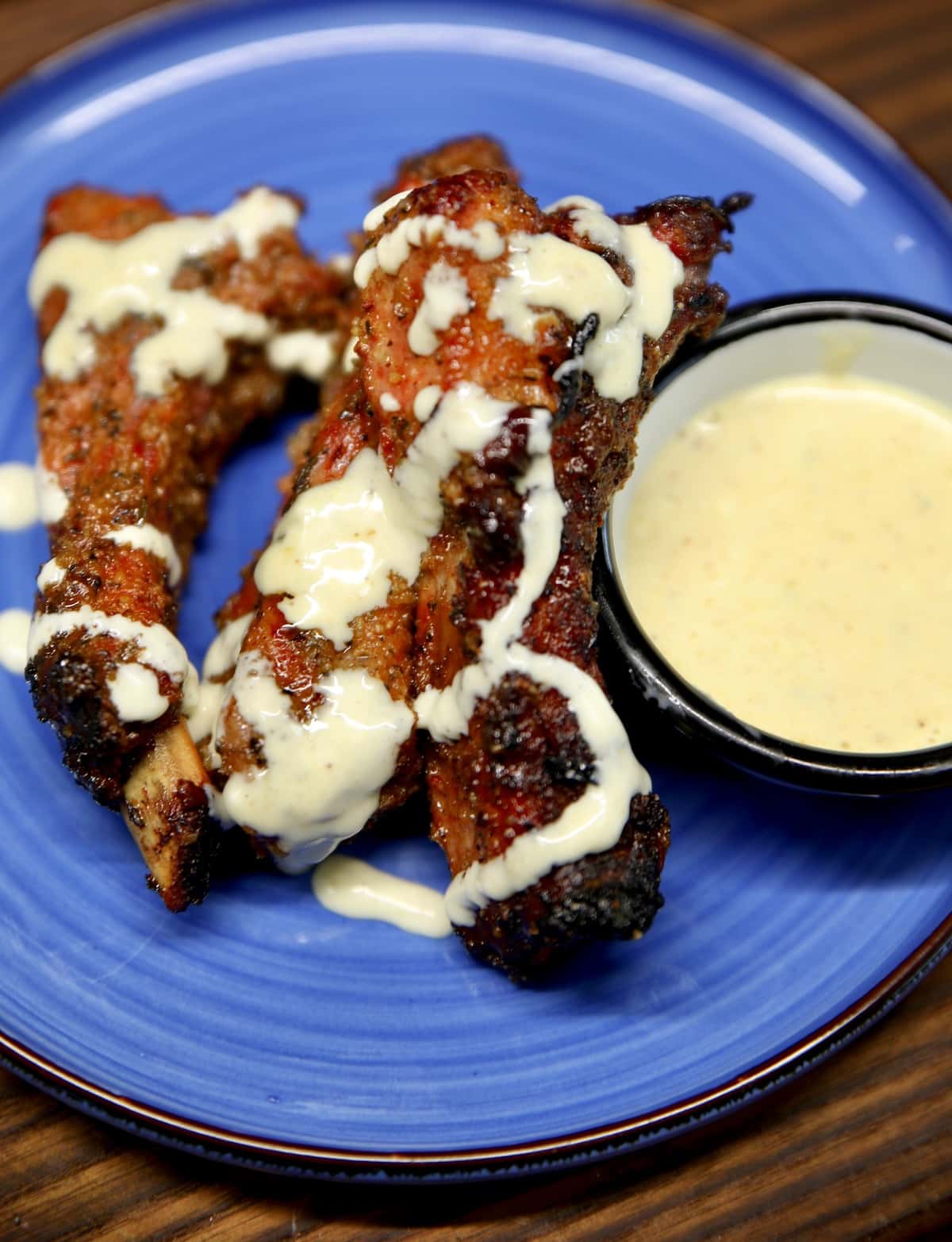 Baby back ribs on a plate drizzled with white bbq sauce.