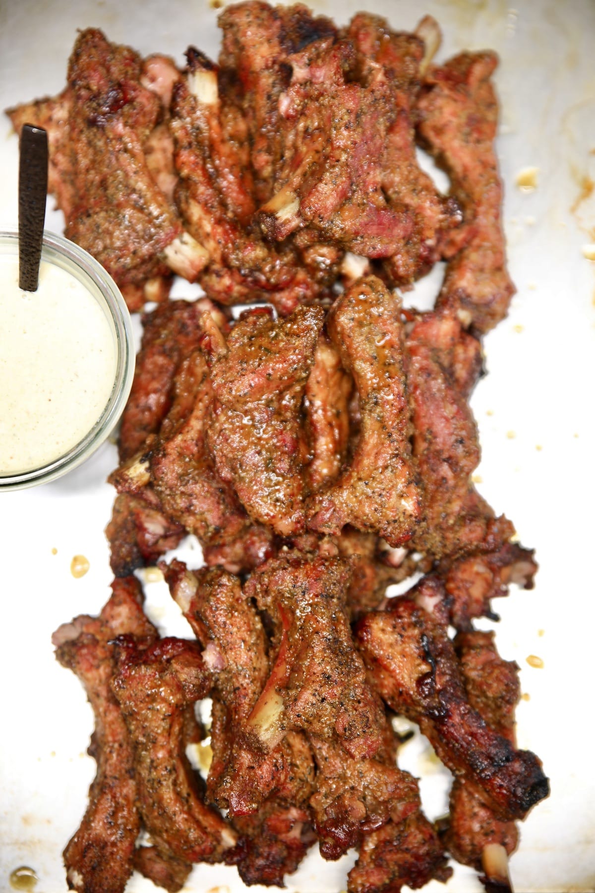 Baby back ribs on a sheet pan, cut apart, jar of white bbq sauce.