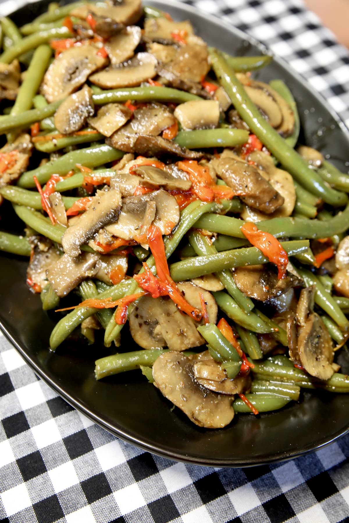 Green beans and mushrooms on a black platter.