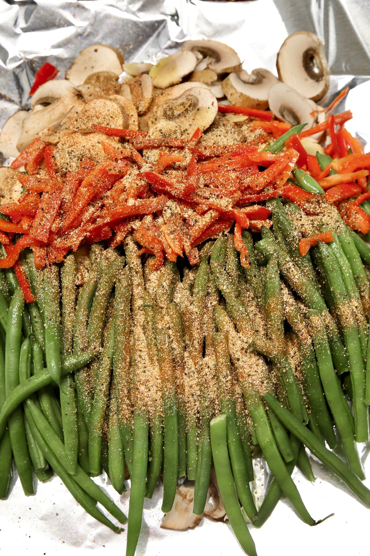 Green beans and vegetables with seasonings on foil.