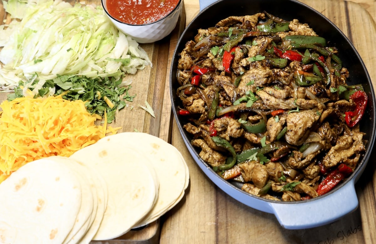 Fajitas on the blackstone. Pan of fajitas, lettuce, cheese, salsa, tortillas.