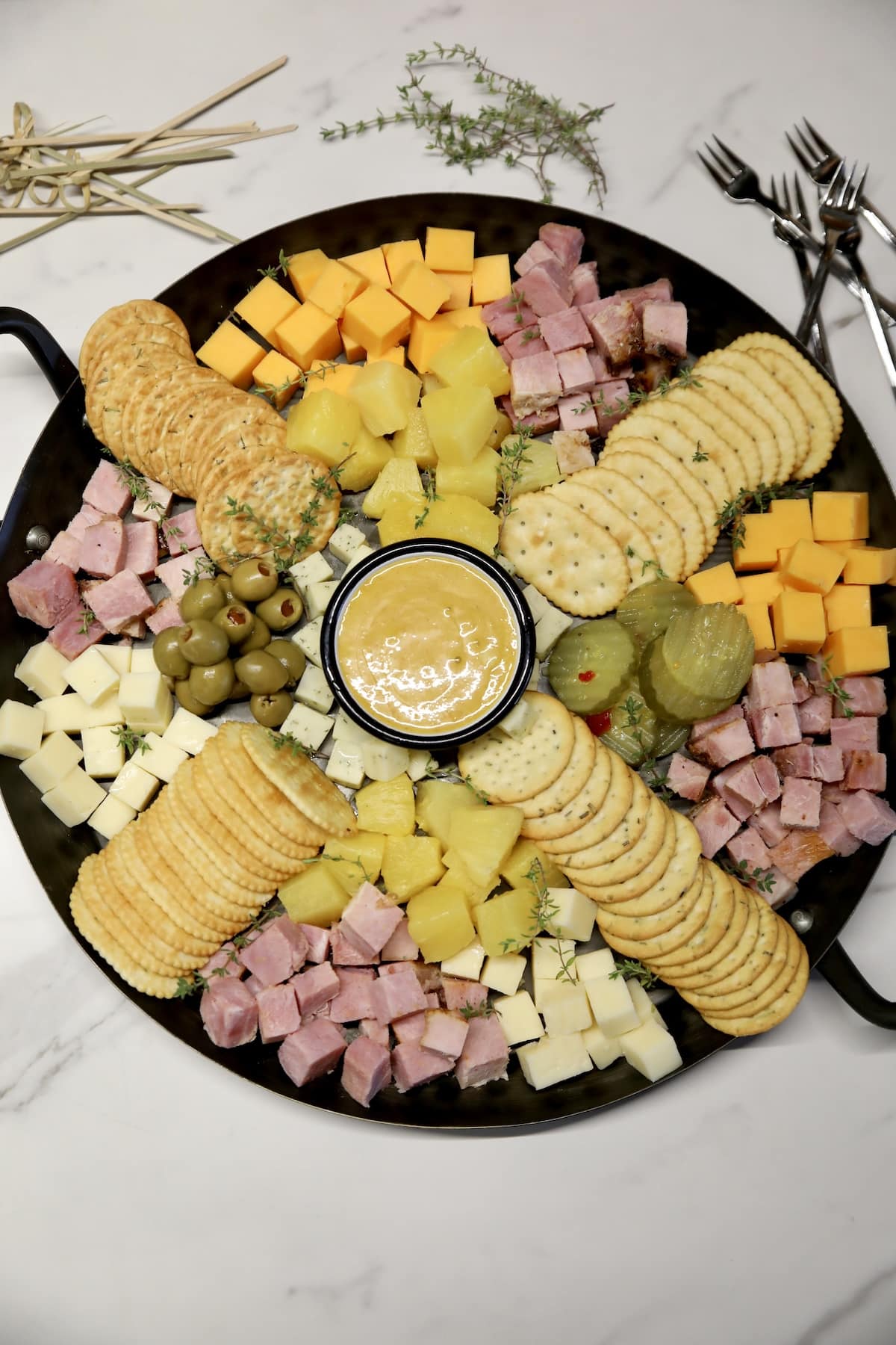 Charcuterie tray with ham, cheese, crackers, pineapple, pickles, olives.