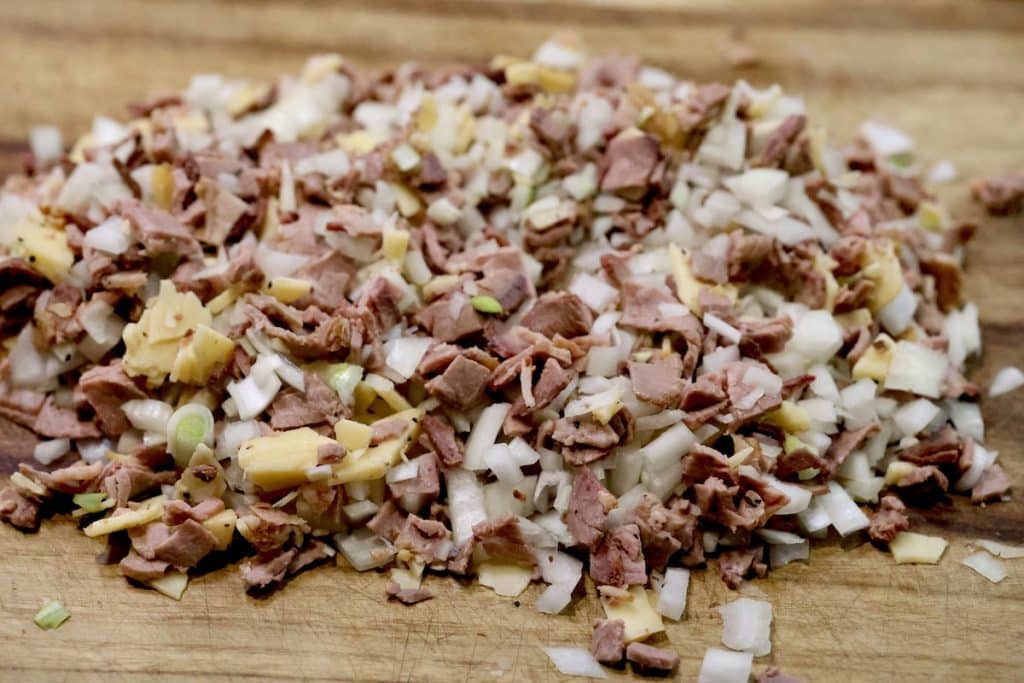 Roast beef chopped with cheese and onions on a cutting board.