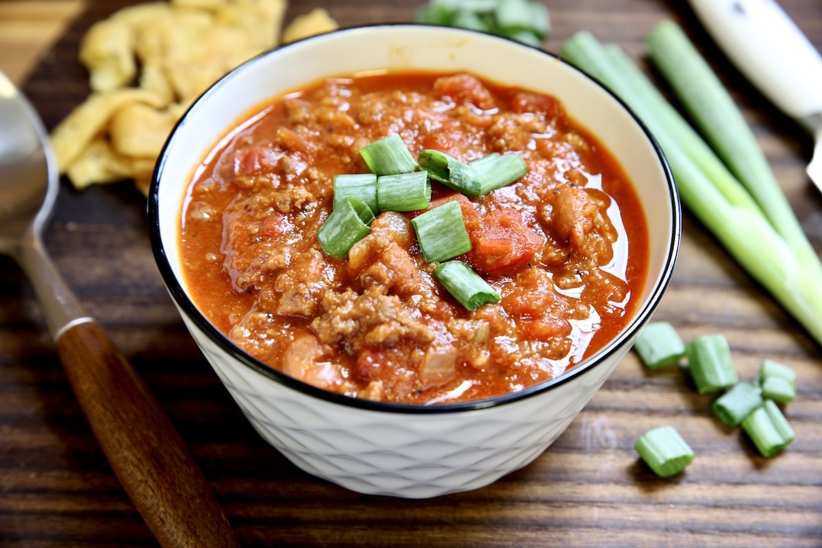 Chili in a bowl with green onion, Fritos on the side.