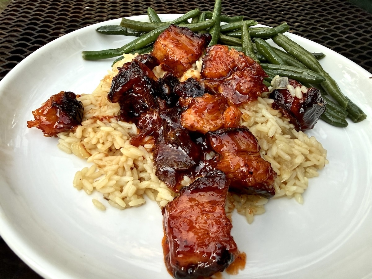 Pork Belly burnt ends on a plate with rice and green beans.